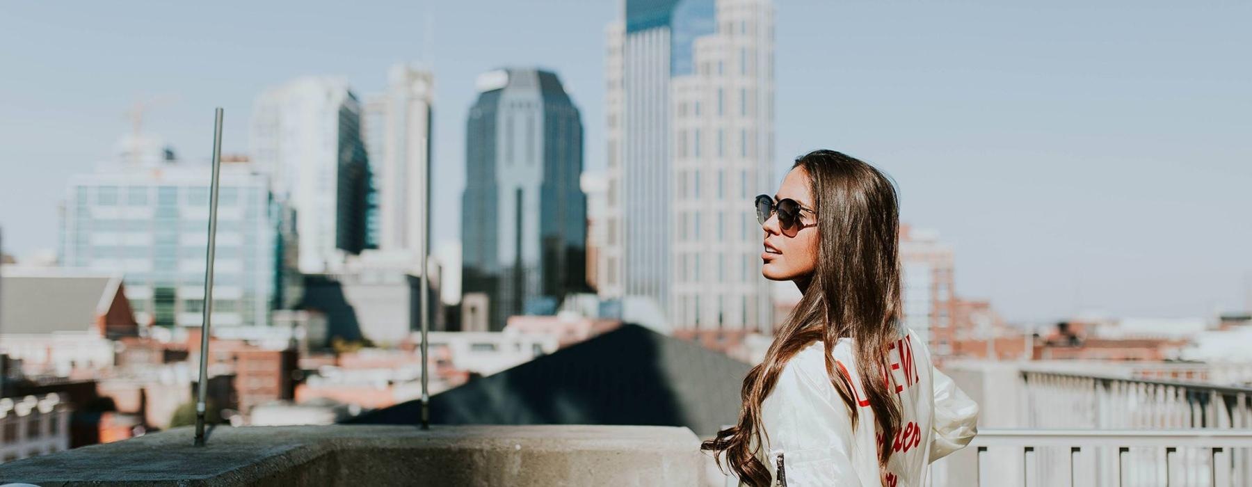 woman with sunglasses stands on a rooftop overlooking the city